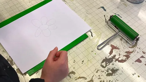 Hand holds paper with flower drawing on table.