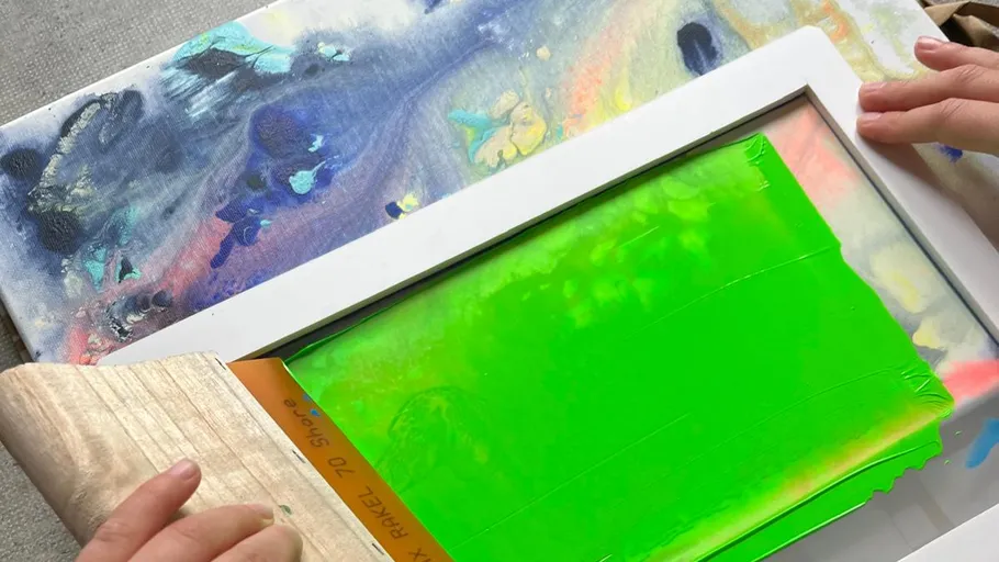 Hands screen printing with green ink on canvas.