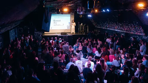 Speaker on stage, audience in dark room.