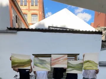 People holding paintings, standing outdoors.