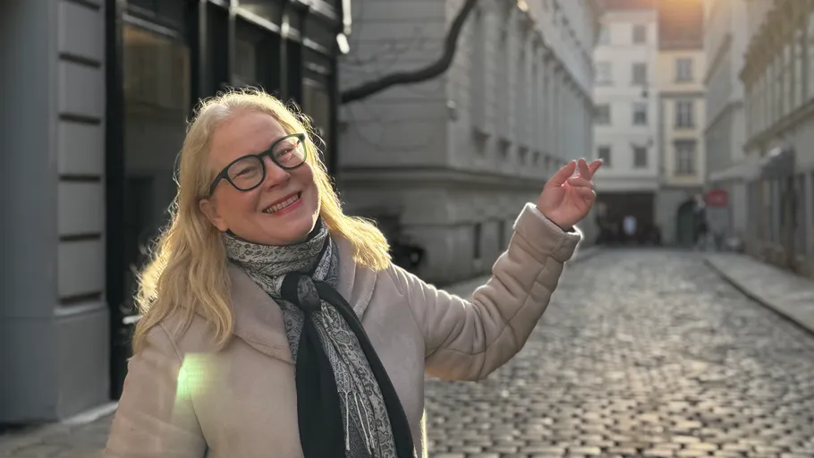 Lächelnde Frau gestikuliert auf Kopfsteinpflasterstraße.