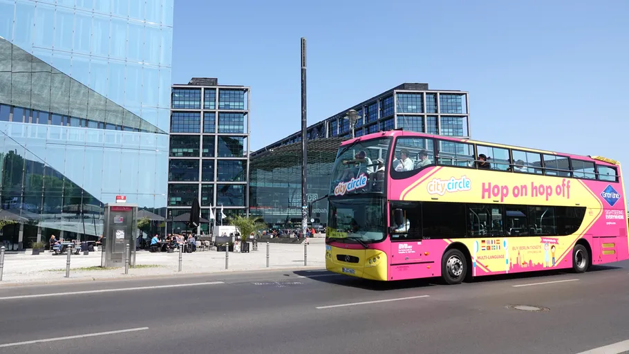 Double-decker tour bus passes modern glass buildings.