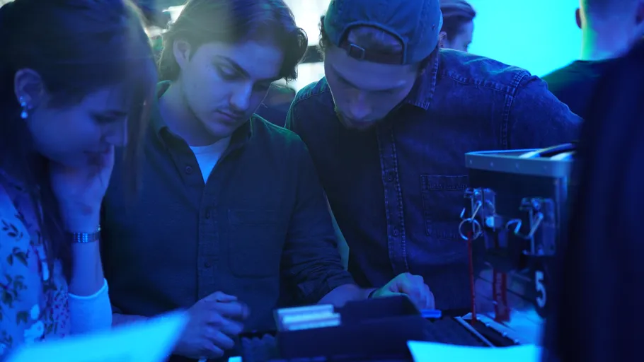 Three people examining a device, blue-lit room.