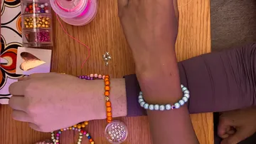 Two arms wearing colorful beaded bracelets.