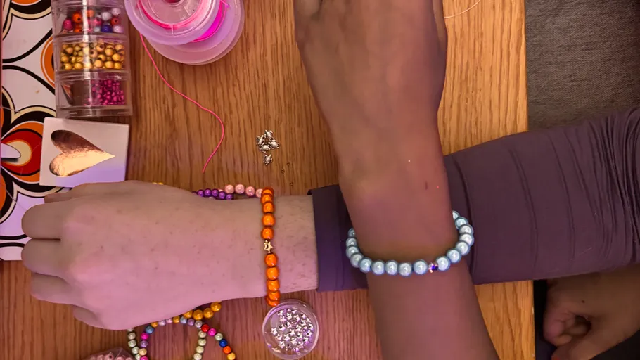 Zwei Arme tragen bunte Perlenarmbänder.