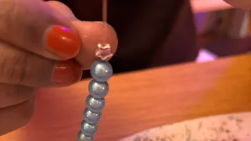 Hand threading blue beads on string, wooden table.
