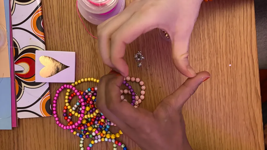 Hände formen Herz über bunten Perlen.