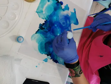 Händed mit Pinsel bemalen blauen Farbklecks auf Papier.