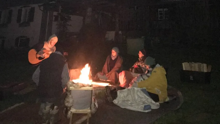 People sitting around campfire with guitar.
