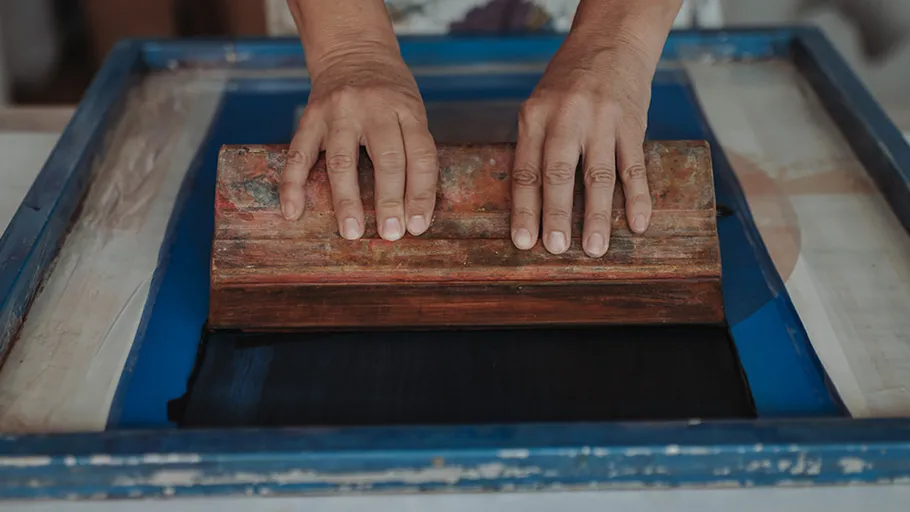 Hände benutzen Rakel im Siebdruck.