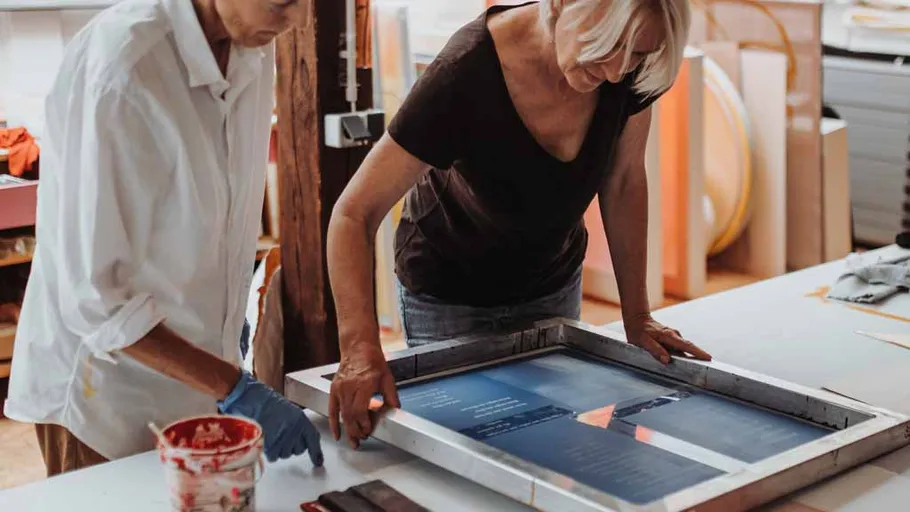 Two people screen printing in workshop.
