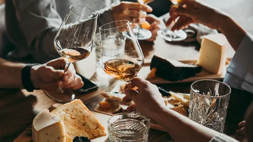 Hands toasting wine glasses over cheese platter.