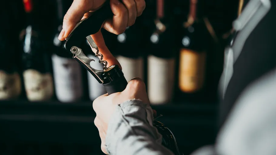 Person opening wine bottle with corkscrew.
