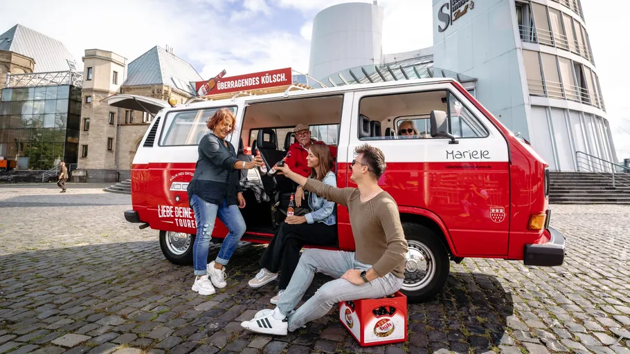 Menschen sitzen am roten Van und teilen Getränke draußen.