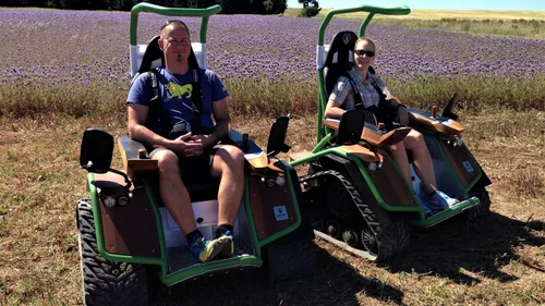 Two people on tracked vehicles in a field.