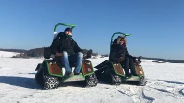 Two people on winter off-road vehicles in snow.