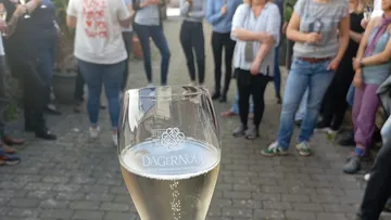 Glass of sparkling wine held among people gathering.