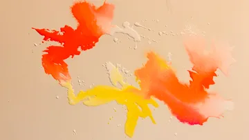 Bunte Farbe spritzt auf beigem Hintergrund.