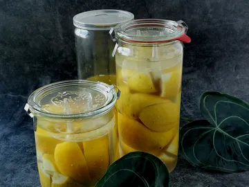 Glass container with preserved lemons on a dark background.