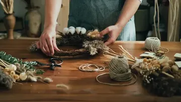 Person bastelt Kranz auf Holztisch.