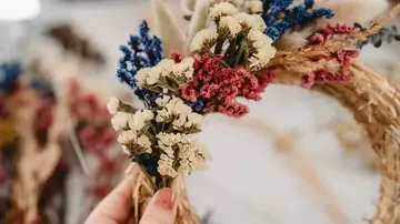 Hand hält bunten Kranz aus Trockenblumen.