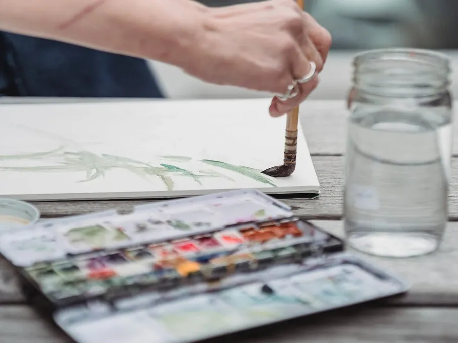 Brush paints green strokes on a piece of paper outside.