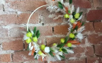 Kranz mit bunten Blumen an Ziegelwand.