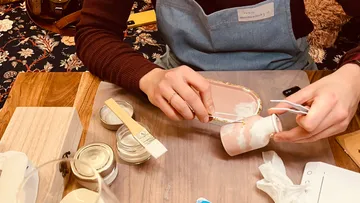 Person decorating small vase with brush, table setting.