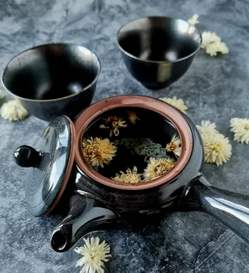 Teapot with flowers surrounded by cups and decor