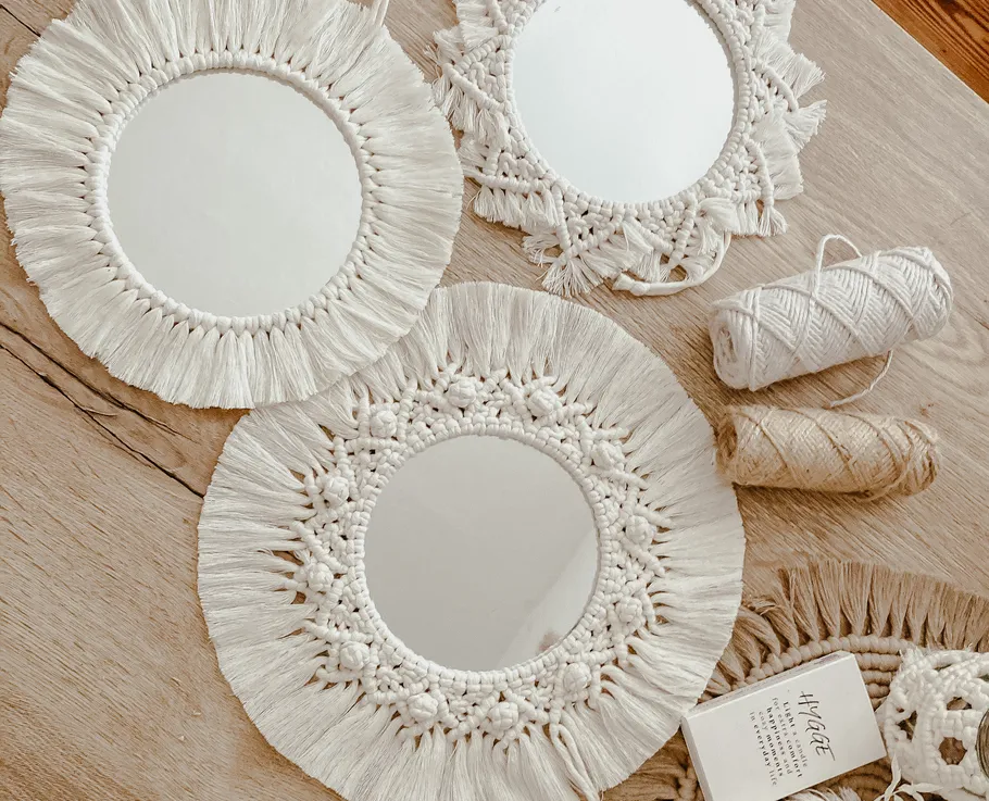 Three macramé mirrors and yarn on wooden floor.