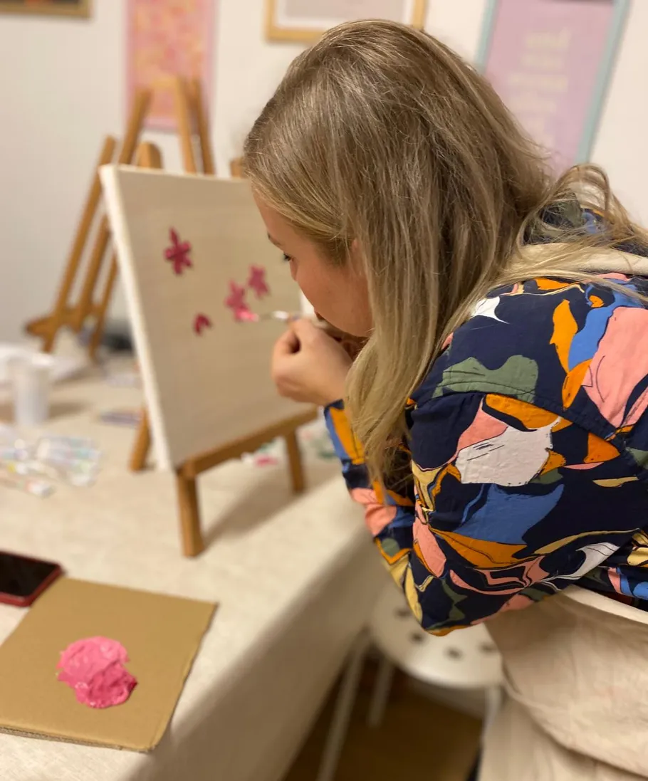 Woman painting flowers on canvas indoors.