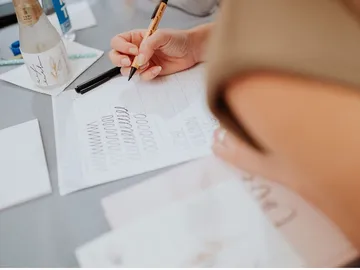 Händed schreibt mit Stift auf Papier, Umgebung ist kreativ.