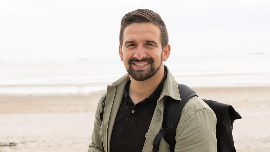 Man smiling with backpack on beach.