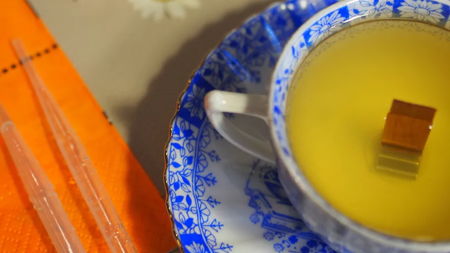 Teacup with yellow liquid on orange napkin.