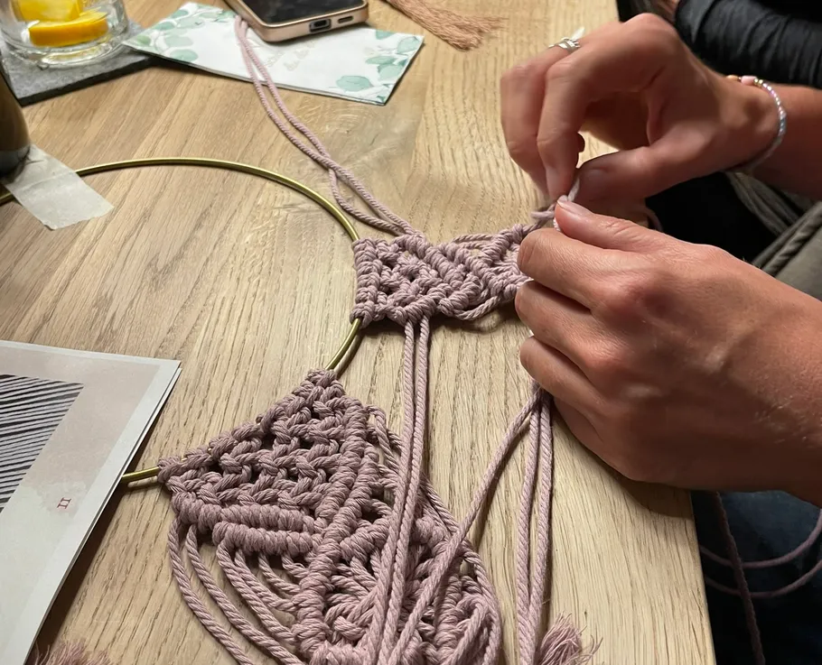 Person fertigt Makramee an einem Holztisch an.