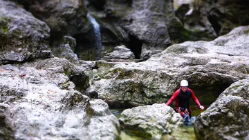 Person macht Canyoning durch felsiges Bachbett.