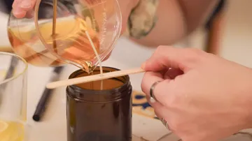 Hands pouring wax into candle jar.
