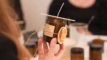 Person hält handgemachte Kerze mit Zitrusdeko.