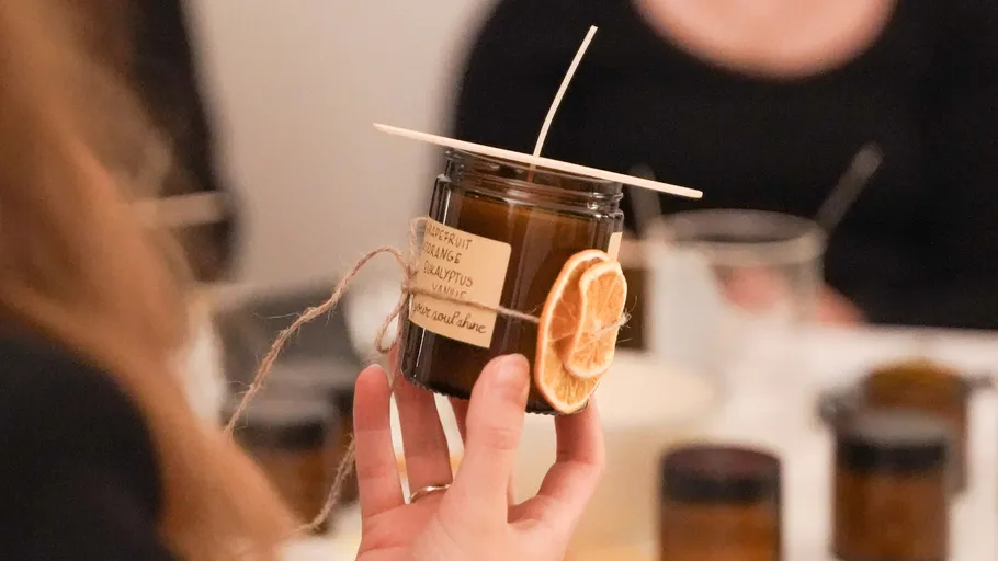 Person holds handmade candle with citrus decoration.