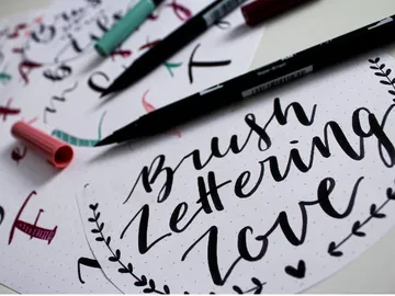 Calligraphy pens lie next to handwritten lettering examples.