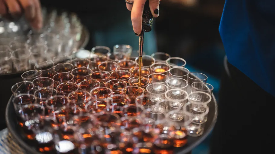 Person pouring drinks into multiple small glasses.