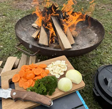 Schneidebrett mit Gemüse neben Outdoor-Feuer.