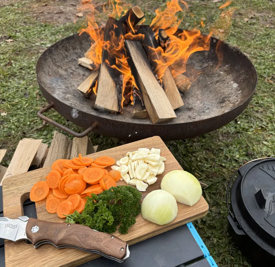 Chopping board with vegetables near outdoor fire.