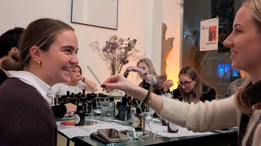 Women smiling, sharing scents at workshop table.