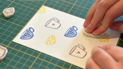 Hand stamping cups on paper, green grid background.
