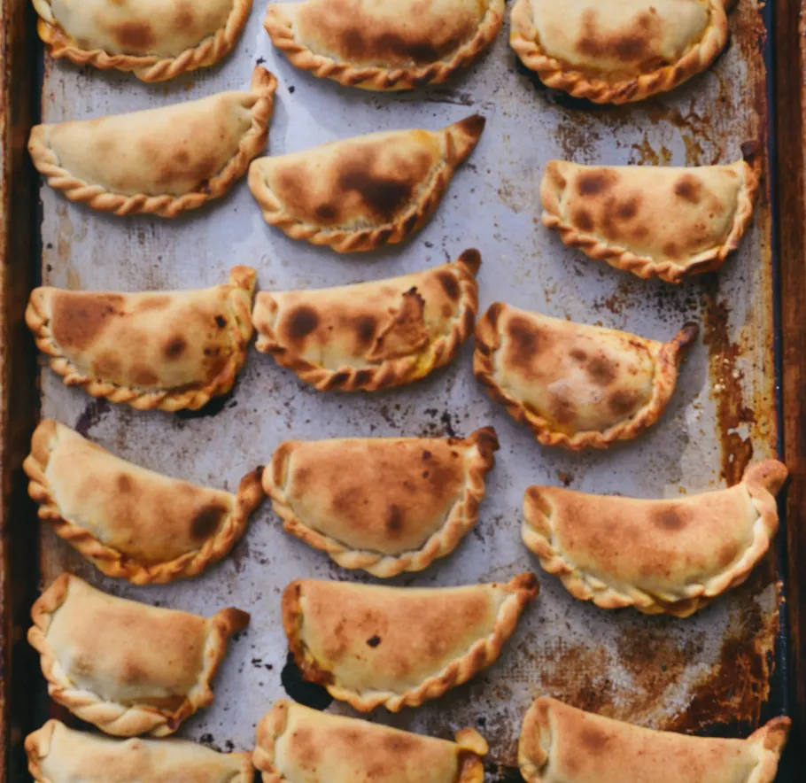 Gebackene Empanadas auf Metall-Backblech angeordnet.