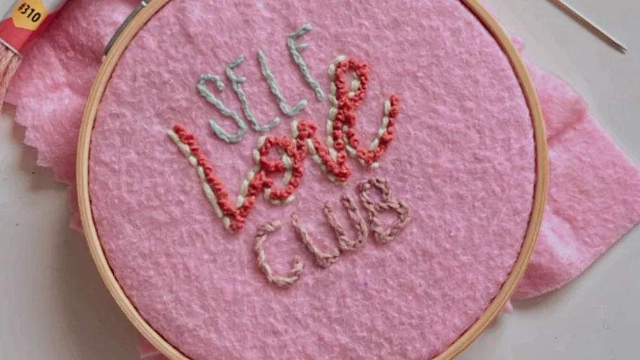 Stickrahmen mit 'Self Love Club' auf rosa Stoff.