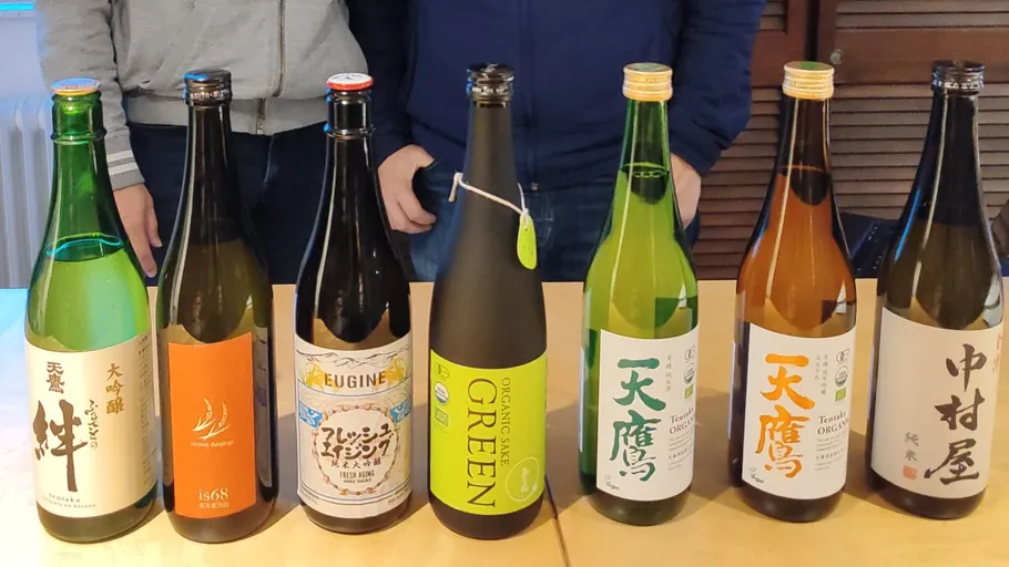 Seven sake bottles on a wooden table.