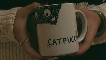 Person hält Tasse mit Katzendesign.