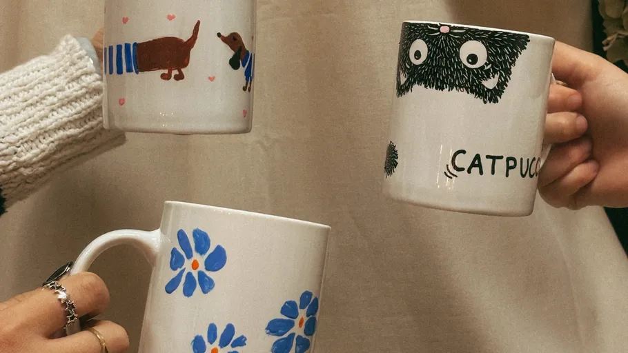 Three mugs with unique designs being held and clinked.